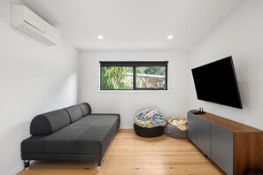 A modern room with a grey sofa, a black bean bag, a wooden cabinet, and a TV mounted on the wall. - Riverside Escape (Anglesea)