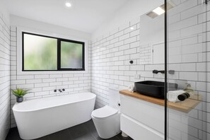 A modern bathroom with a freestanding bathtub, a toilet, and a window.