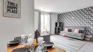 A modern living room with a dining area, grey sofa, geometric patterned wall, and a framed inspirational quote. - TheBlueStay 134 - Cozy Apartment in Bagnolet (Paris)