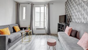 A modern living room with two grey sofas, a small round table, a television on a stand, and a patterned wall. - TheBlueStay 134 - Cozy Apartment in Bagnolet (Paris)
