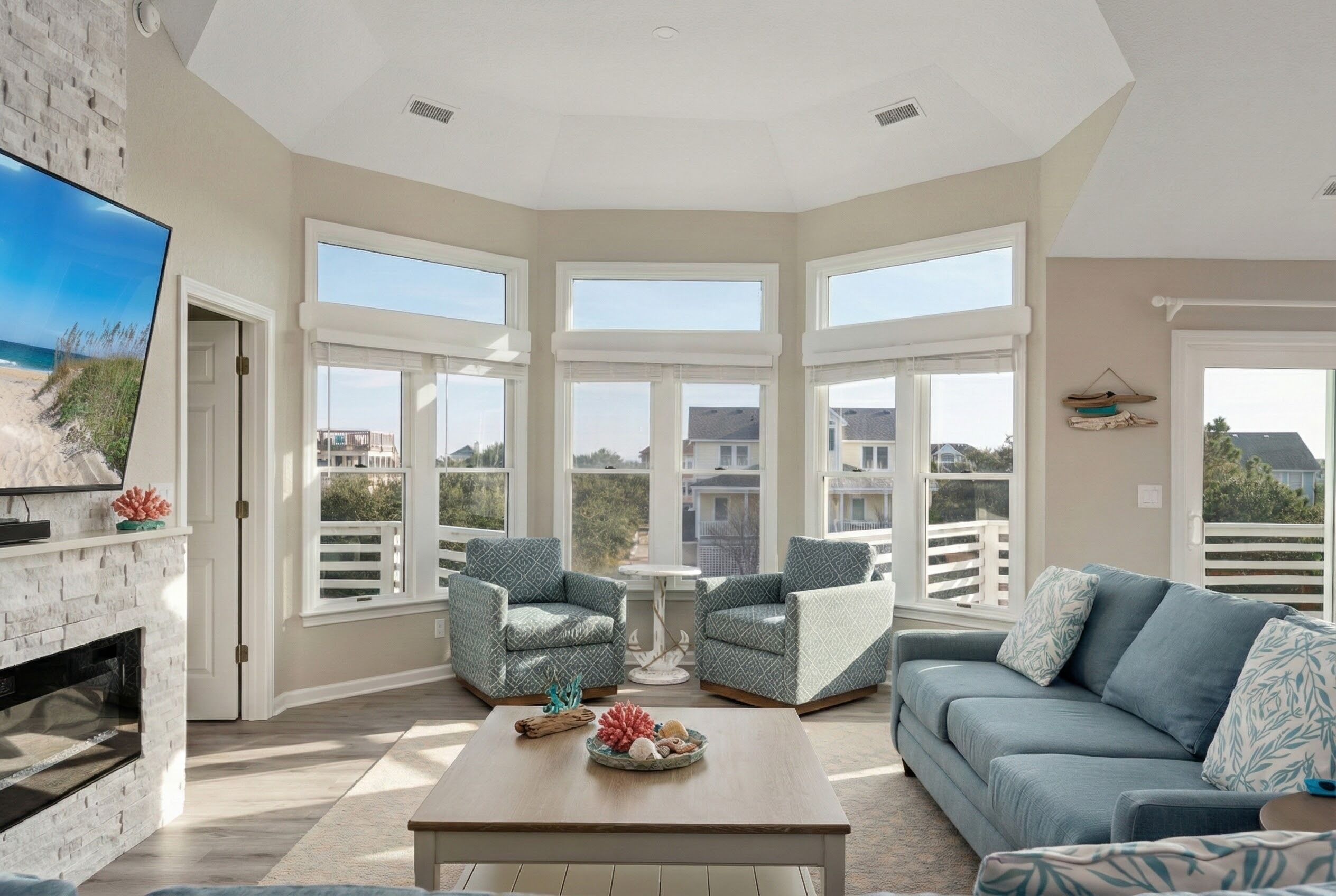 A spacious living room with a fireplace, large windows, and a view of the beach.