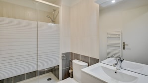 A modern bathroom with a glass-enclosed shower, a toilet, and a sink with a mirror.