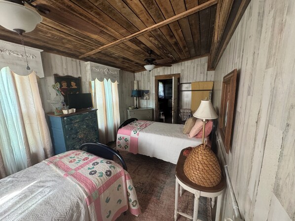 Una habitación rústica con vigas de madera en el techo, dos camas con ropa de cama floral, un tocador, una lámpara y una cesta tejida.