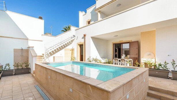 Une piscine avec une terrasse ensoleillée, un escalier et un espace repas aménagé avec du mobilier d’extérieur.