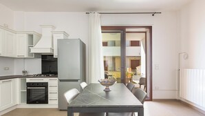 Une cuisine moderne avec des meubles blancs, une table à manger avec des chaises, un four encastré et un réfrigérateur.