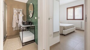 Une salle de bain moderne avec une douche, un lavabo et un miroir. On y trouve un porte-serviettes avec des serviettes, une petite table avec un bol, et un mur d’accent de couleur verte.