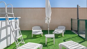 A rooftop terrace with artificial grass, white lounge chairs, a white umbrella, and a metal ladder.