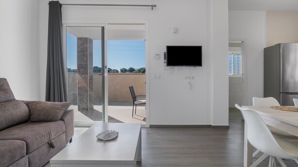 A modern living room with a sofa, a coffee table, a TV mounted on the wall, and a sliding glass door leading to an outdoor area.