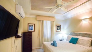 Et hotelværelse med seng, fjernsyn ophængt på væggen, kommode og ventilator.