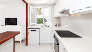 A modern kitchen with white cabinetry, a built-in oven, a dishwasher, and a window with a view of greenery.