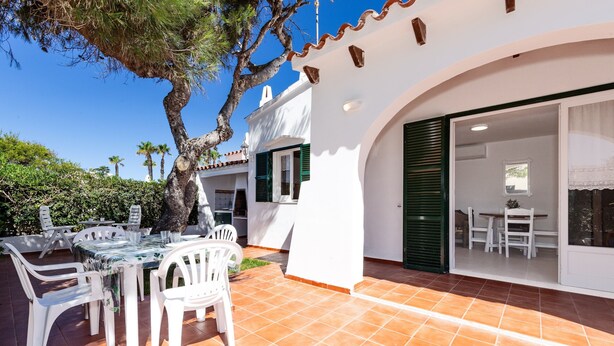 A white building with a tiled patio, outdoor seating, and a tree.