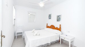 A white room with a bed, a wooden headboard, a nightstand, a white chair, and a ceiling fan.