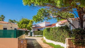 A residential street with houses, a paved path, and a green fence.