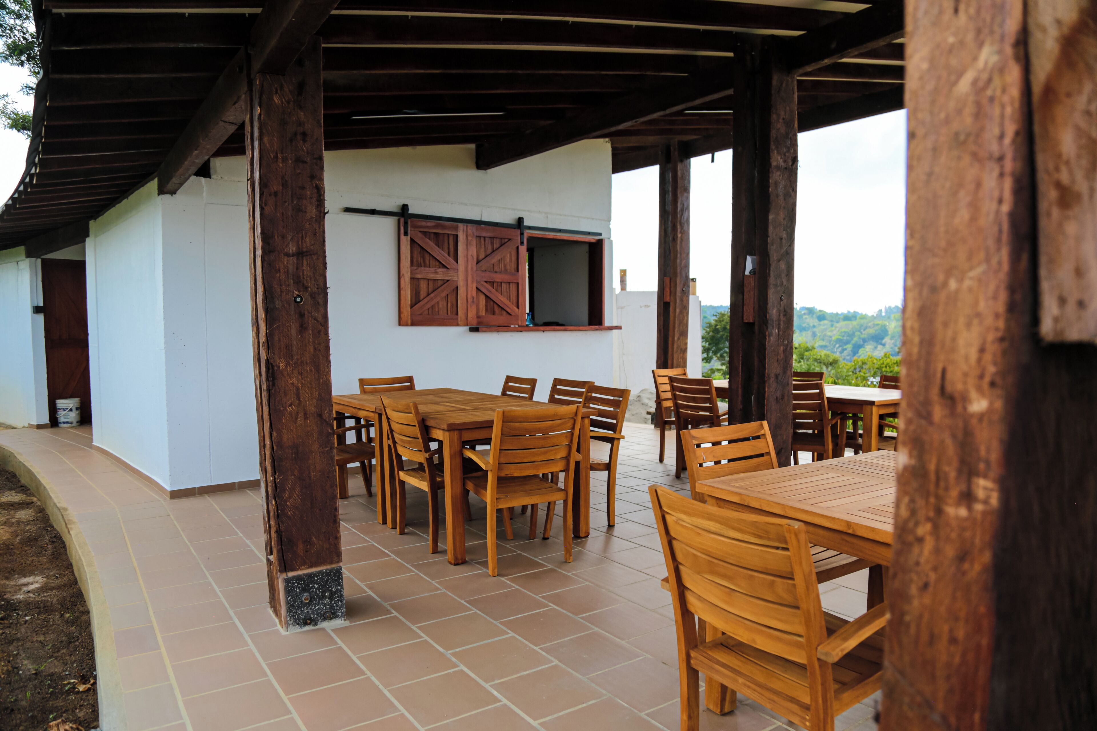Une terrasse extérieure avec des tables et des chaises en bois, un plafond en bois et un mur blanc avec une fenêtre.