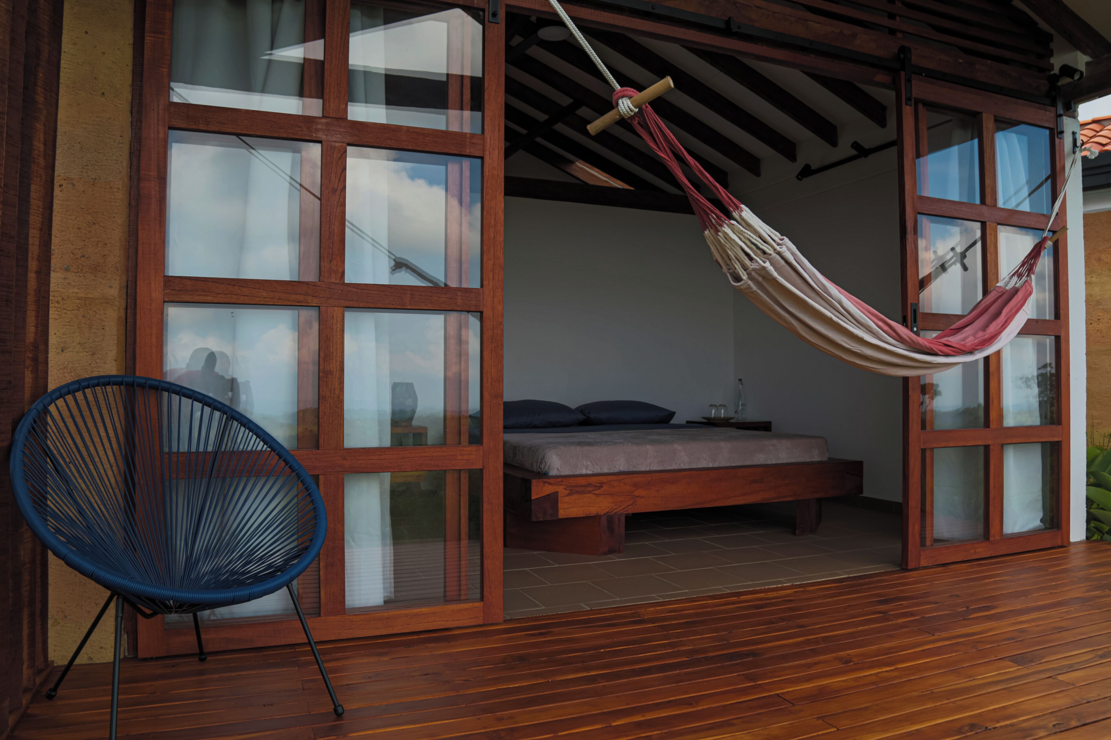 Une pièce avec un plancher en bois, un lit avec un matelas et des oreillers, un hamac et une chaise bleue.