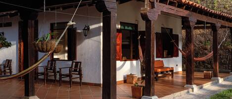 A covered patio with wooden furniture, a hammock, and potted plants.