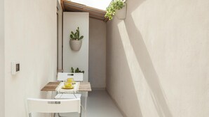 Um pequeno espaço ao ar livre cercado, com uma mesa e cadeiras brancas, uma planta pendurada e um cacto em vaso.