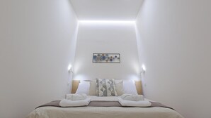 Quarto de hotel com cama, cabeceira, obra de arte na parede e iluminação embutida no teto.