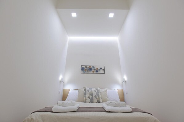 A hotel room with a bed, a headboard, a wall-mounted artwork, and recessed ceiling lighting.