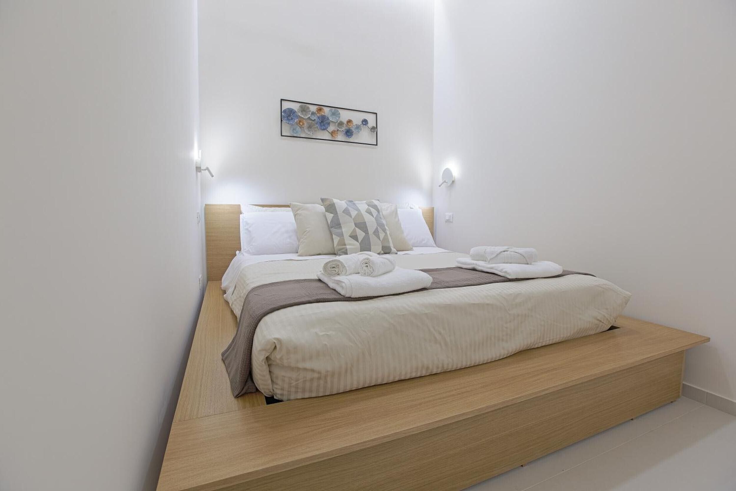 Une chambre à coucher avec un lit, des oreillers, une couverture et une œuvre d’art accrochée au mur.