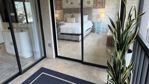 A bedroom with a large sliding glass door leading to a balcony, a bedside table with a lamp, and a potted plant. - Modern 2 Bedroom Condo in Prime Gulf-Front Community with Pool, Wifi, AC & More (Tarpon Springs)