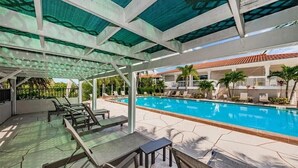 An outdoor pool area with lounge chairs and a covered seating area. - Modern 2 Bedroom Condo in Prime Gulf-Front Community with Pool, Wifi, AC & More (Tarpon Springs)
