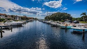 A marina with boats docked along a calm waterway, surrounded by buildings and greenery. - Modern 2 Bedroom Condo in Prime Gulf-Front Community with Pool, Wifi, AC & More (Tarpon Springs)