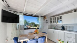 Een keuken met een eettafel, stoelen, een televisie, kasten en een raam met gordijnen.