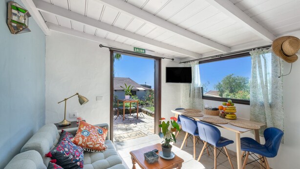 Een kamer met een bank, een tafel met stoelen, een televisie en uitzicht op het exterieur.