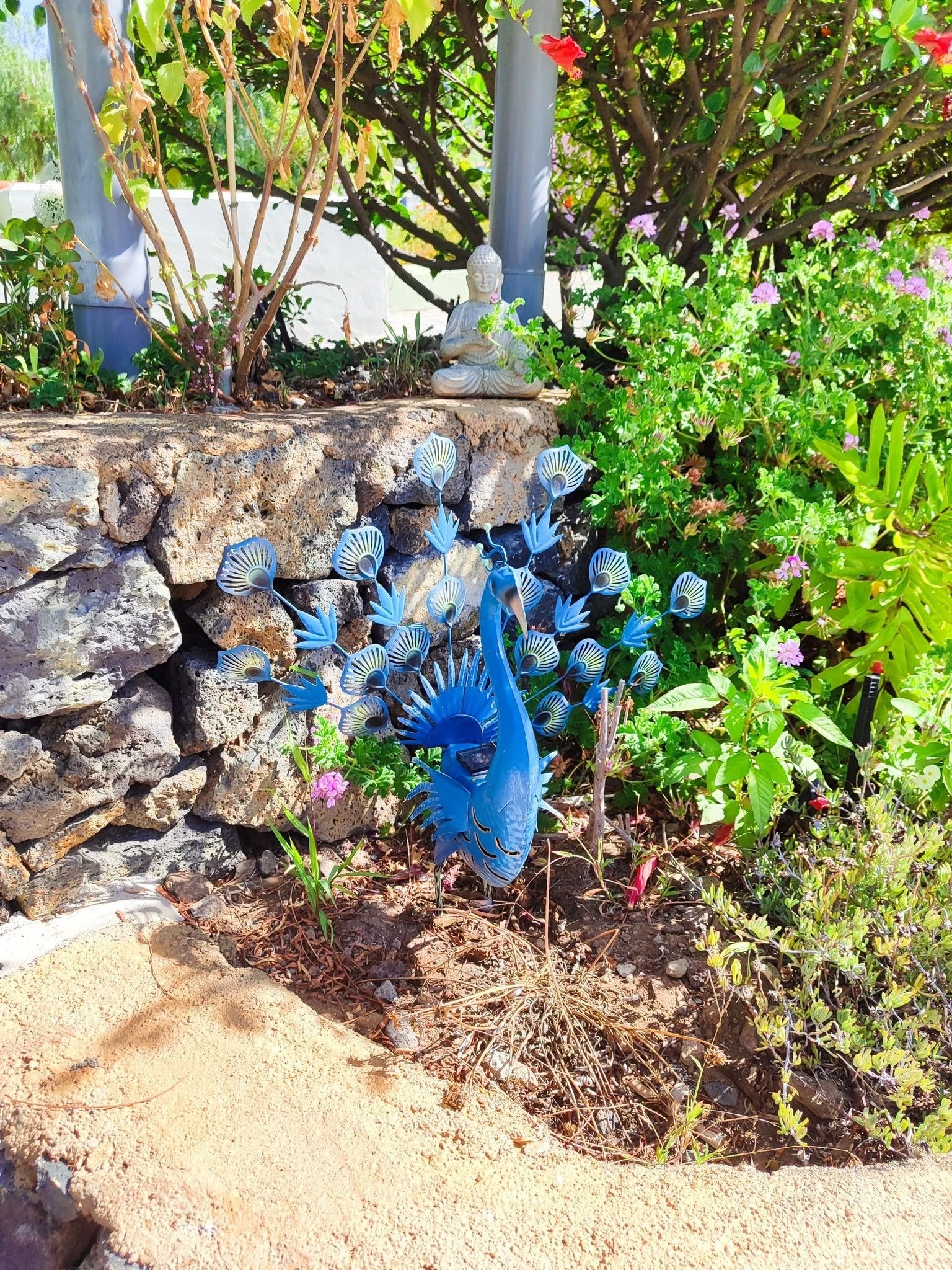 A garden with a stone wall, a Buddha statue, and a blue bird sculpture.