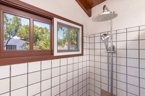 A bathroom with a shower, a window with a brown frame, and tiled walls.