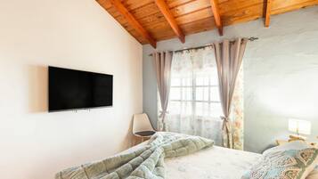 A bedroom with a bed, a chair, a TV, and a window with curtains.