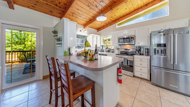 Een keuken met een houten plafond, een groot eiland met barstoelen, roestvrijstalen apparatuur en uitzicht op groen buiten.