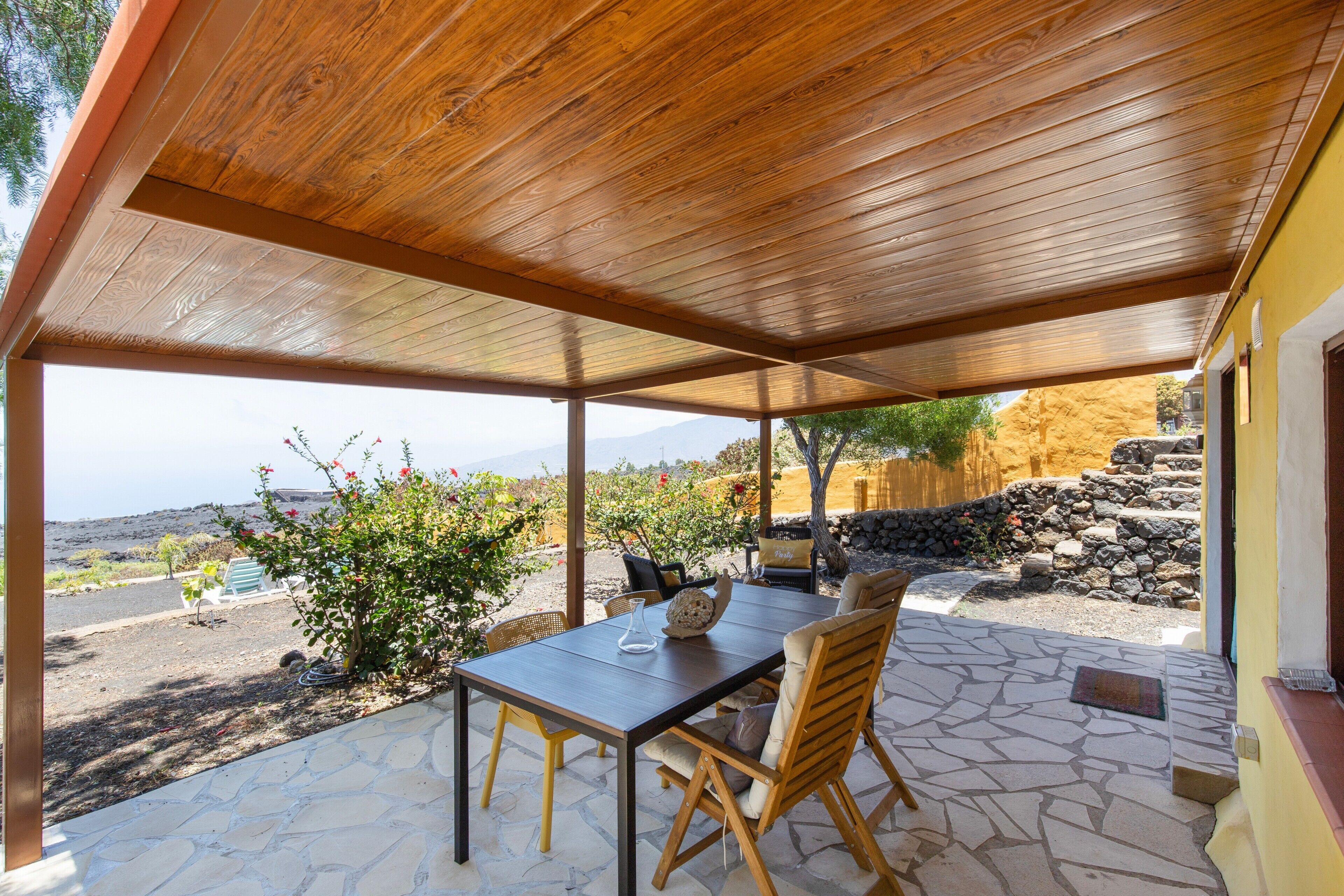 A covered patio with a table and chairs, a stone floor, and a view of the landscape.