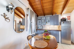 Una cocina con techo de madera, una mesa de comedor con individuales tejidos, un frutero y un refrigerador.