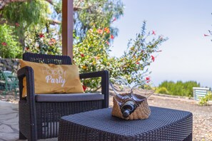 A wicker chair with a 'Happy Party' pillow, a glass bottle, and a woven basket on a woven table.