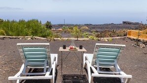 Two white lounge chairs facing a table with a vase and two mugs, set on a terrace with a view of a volcanic landscape. - Holiday Home 'El Perenquén' with Mountain View, Wi-Fi and Air Conditioning (Los Llanos de Aridane)