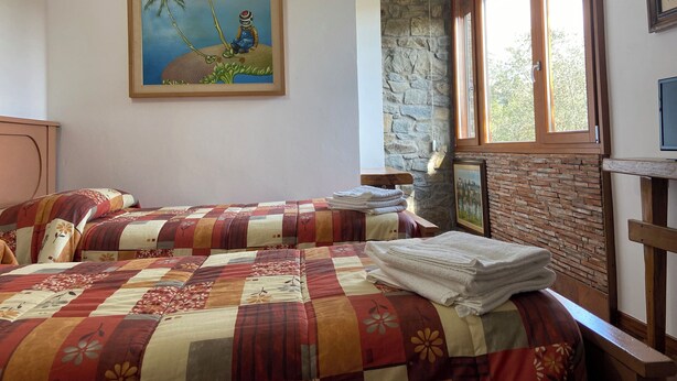 Un dormitorio con dos camas, una pared de piedra, un cuadro de una escena tropical y una ventana con vistas a árboles.