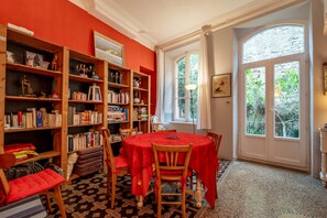 Uma biblioteca com estantes, uma mesa redonda com cadeiras e uma janela grande.