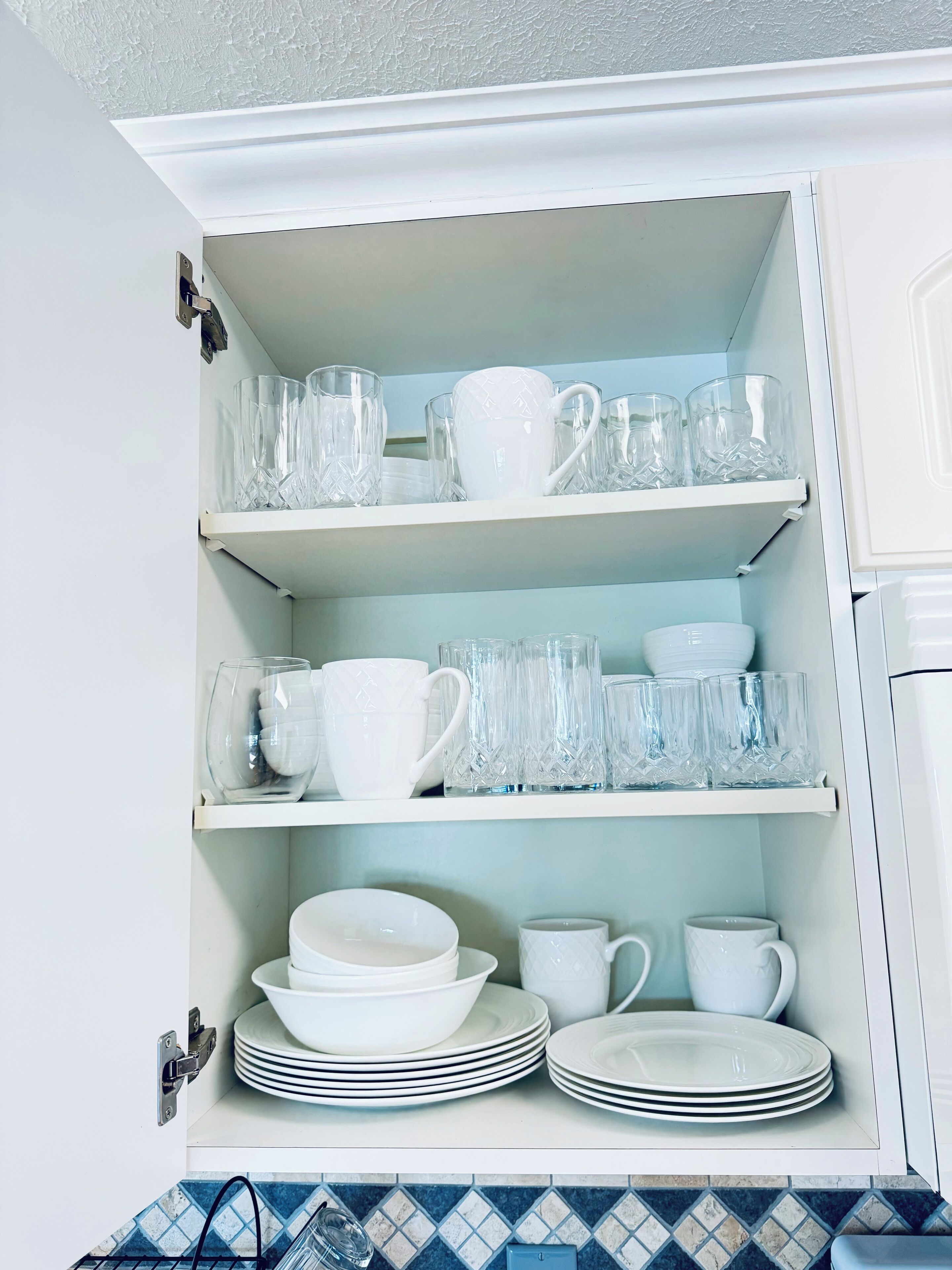 Et skab med flere hylder fyldt med forskelligt glas og hvide tallerkener.