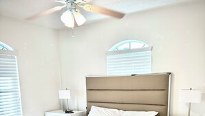 A neatly made bed with rolled towels, a ceiling fan, and a nightstand with a lamp.