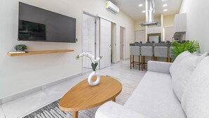 A modern living room with a sofa, a coffee table, a TV, and a kitchen area in the background. - 2 BD Suite w/ Balcony, Gym + Rooftop Pool (Playa del Carmen)