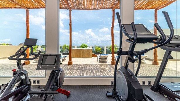 A gym with exercise equipment and a view of a pool and lounge area. - 2 BD Suite w/ Balcony, Gym + Rooftop Pool (Playa del Carmen)