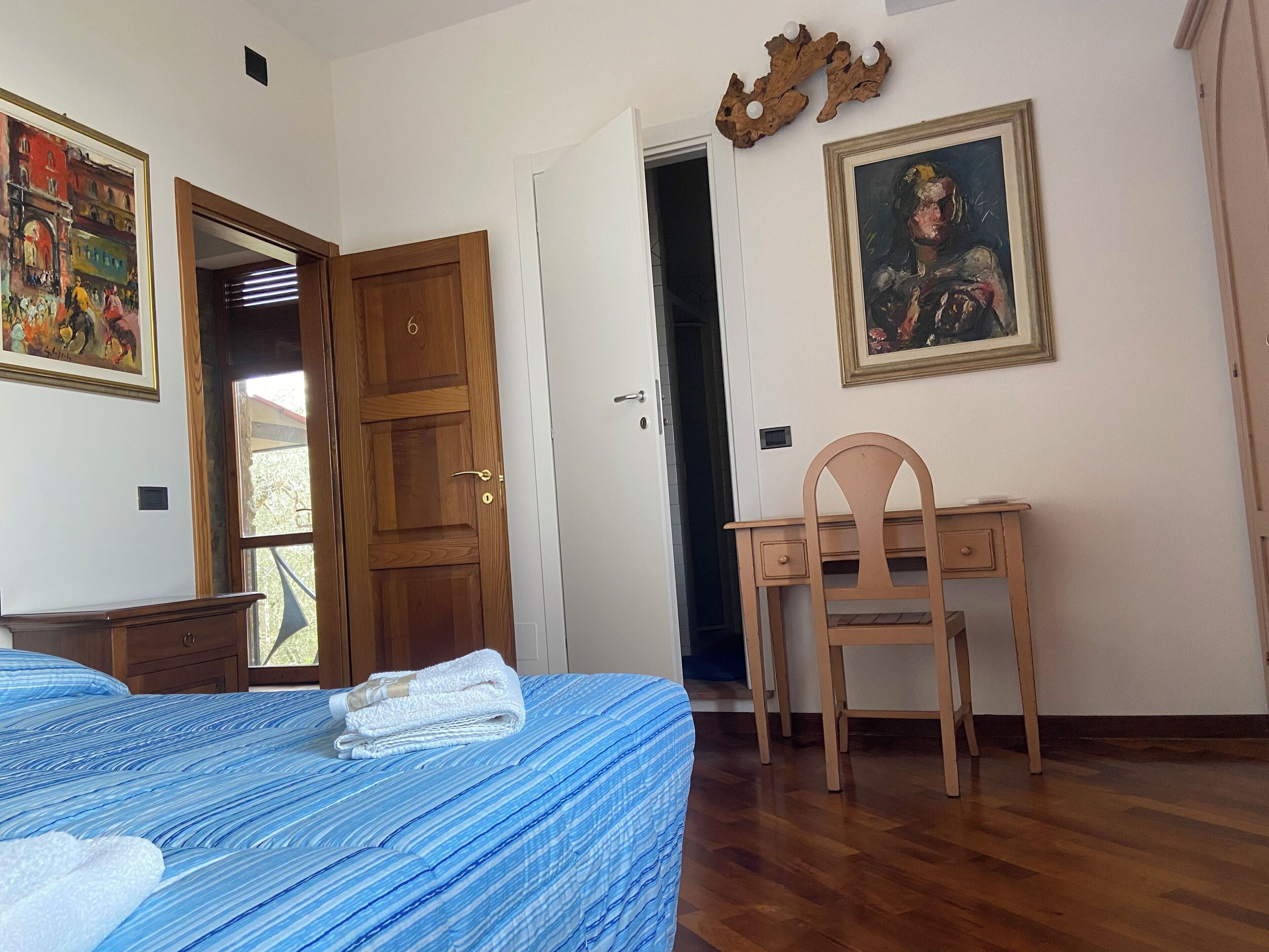 A bedroom with a bed, a wooden desk, a chair, a door, and a painting on the wall.