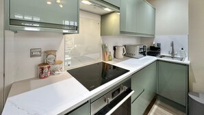 Una cocina moderna con estufa integrada, microondas y lavaplatos, que presenta gabinetes verde claro y encimeras blancas.