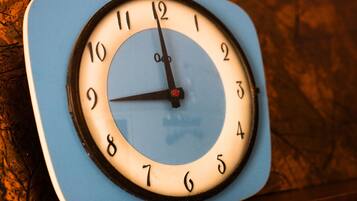 Un reloj de pared cuadrado con esfera azul y blanca, que muestra los números del 1 al 12 y un segundero.