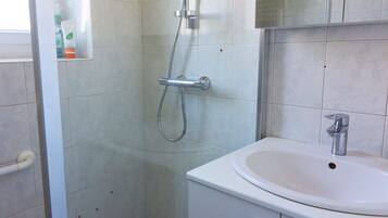 Un baño con ducha, lavamanos y armario.