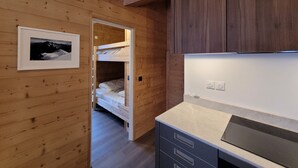 A wooden room with a bunk bed, a framed picture on the wall, and a kitchenette area with cabinets and a countertop. - Beautiful new T3 1km from the slopes (Le Monêtier-les-Bains)
