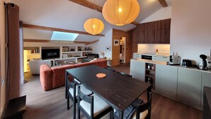 A modern kitchen with wooden cabinets, a dining area with a dark wooden table and chairs, and a cozy living space with a sofa and a television. - Beautiful new T3 1km from the slopes (Le Monêtier-les-Bains)