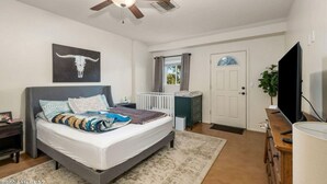 Un dormitorio con cama, ventilador de techo, televisión, una puerta y una ventana.